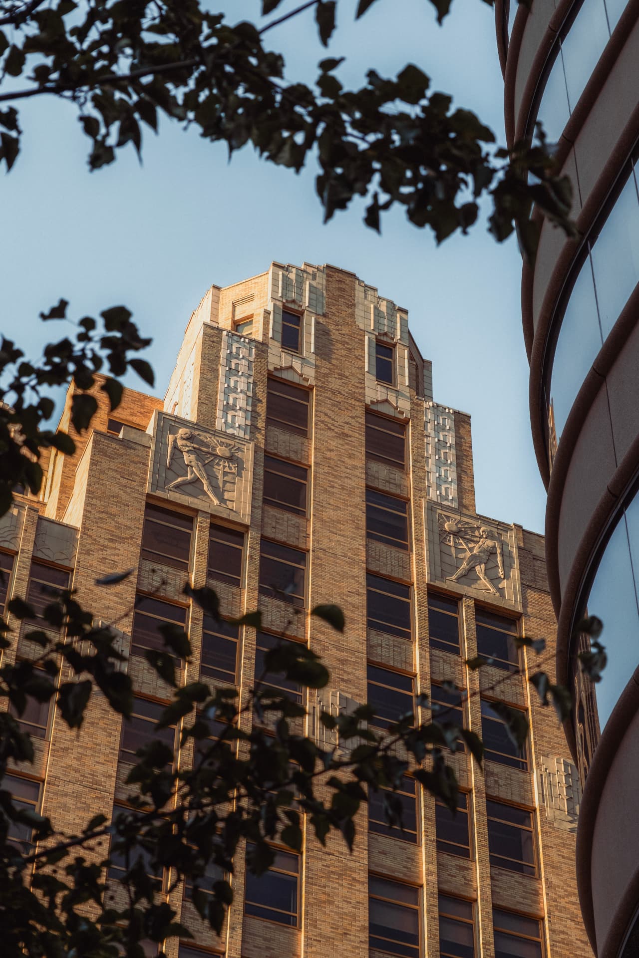 Art Deco brick crown of 345 Hudson Street in Manhattan lit by late afternoon sun, framed by tree leaves